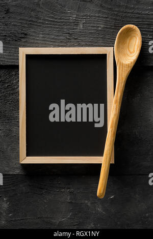 Blank, empty, black chalkboard with wooden cooking spoon flat lay from above on black wooden table with copy space Stock Photo