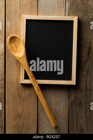 Blank, empty, black chalkboard with wooden cooking spoon flat lay from above on brown wooden table with copy space Stock Photo