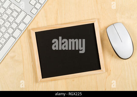 Empty, blank, black chalkboard with computer mouse and keyboard on brown wooden table flat lay from above with copy space - e-learning or computer sci Stock Photo