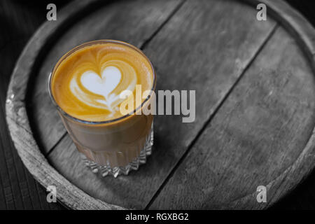 A cup of coffee with a heart latte foam art on top, sitting on a wooden tray, in black and white, monochrome. Stock Photo