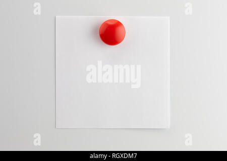 Square blank sheet of white paper pinned with a red button magnet on white refrigerator Stock Photo