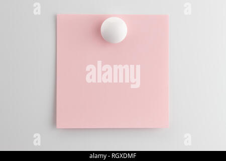 Square blank sheet of pink paper pinned with a white button magnet on white refrigerator Stock Photo