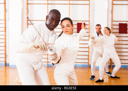 Female fencer practicing  movements with african american male trainer at workout Stock Photo