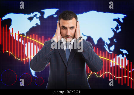 Worried broker holding both hands on ears as not-hearing bad news or financial crisis concept on background with decreasing economy graph Stock Photo