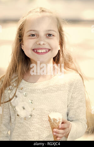 Girl sweet tooth on happy face eats ice cream, light background. Kid girl with ice cream cone in hand. Summer treats concept. Sweet tooth girl child with white ice cream in waffle cone. Stock Photo