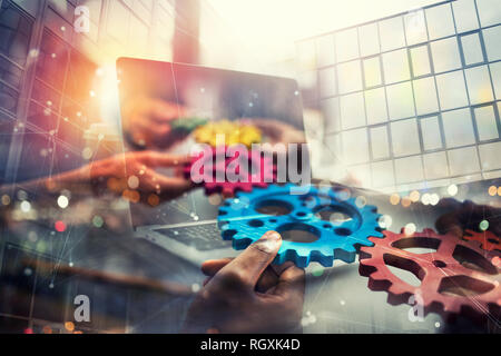 Business people with gears in hand that exit from a laptop. concept of remote cooperation and teamwork. Double exposure Stock Photo