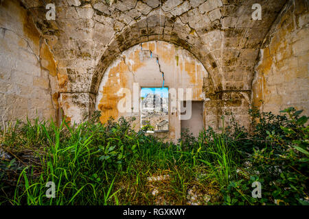 View through a window of a medieval, cracked stone wall of the ancient Madonna de Idris rock church and Sassi of Matera, Italy, in Basilicata region Stock Photo