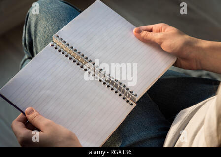 Woman holding spiral bound notebook with lined paper in lap, sitting in sunlight Stock Photo
