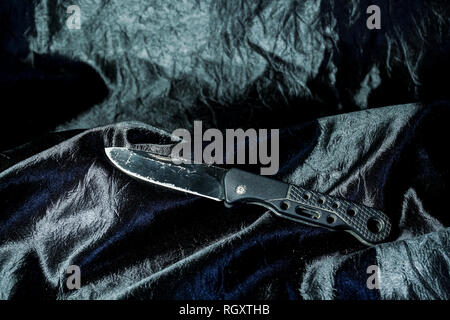 The old black folding knife on the black fabric is shiny. Stock Photo