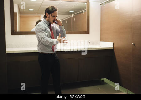 Furious Business Man Screaming On Cell Phone In Office Restroom Stock Photo