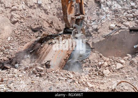 On a demolition site the bucket of an excavator pulls a concrete slab, remains of foundation of a building. Stock Photo