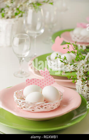 Happy easter. Decor and table setting of the Easter table - Branches of flowering spring tree, dishes of pink and green color. Selective focus. Stock Photo
