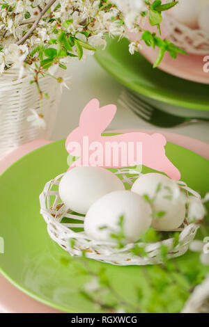 Happy easter. Decor and table setting of the Easter table - Branches of flowering spring tree, dishes of pink and green color. Selective focus. Stock Photo