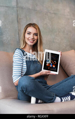 adult girl sitting on sofa and showing screen of digital tablet Stock Photo