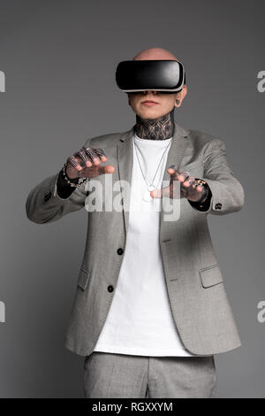 bald tattooed man in suit using virtual reality headset isolated on grey Stock Photo