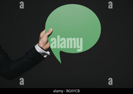 cropped view of man holding green speech bubble in hands isolated on black Stock Photo