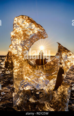 Glacier and balanced rocks with sun star on Iceland's Diamond Beach with black sand next to Glacier Bay Stock Photo