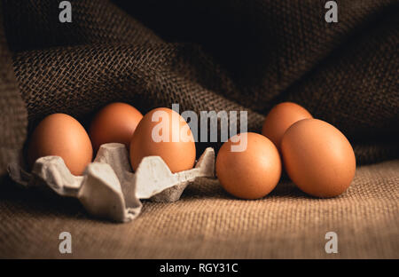 Photo of raw illuminated eggs  in kitchen with jute on dark background. Close-up photography of bio chicken eggs in egg box . Stock Photo
