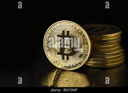 Bitcoin: Physical bit coin aslo called Digital Currency or Cryptocurrency, on edge standing in front of a stack, on black with reflection and copy spa Stock Photo