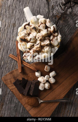 Overhead shot of a mug of hot cocoa with toasted marshmallows next to a cutting board with chocolate chunks and cinnamon sticks. Vertical Format - Sha Stock Photo