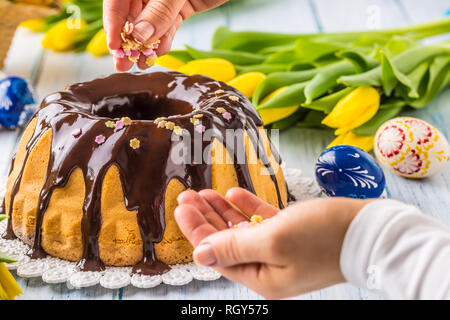 Delicious holiday slovak and czech cake babovka with chocolate glaze.Female hands decorating a cake.  Easter decorations - spring tulips and eggs. Stock Photo