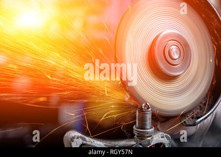 Close-up on the sides fly bright sparks from the angle grinder machine. A young male welder in a white working gloves grinds a metal product with angl Stock Photo