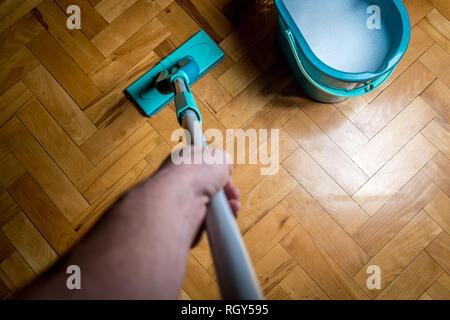 Wiping dirty wooden floor by wet wiper mop, housework. Man cleaning the house. Topview Stock Photo