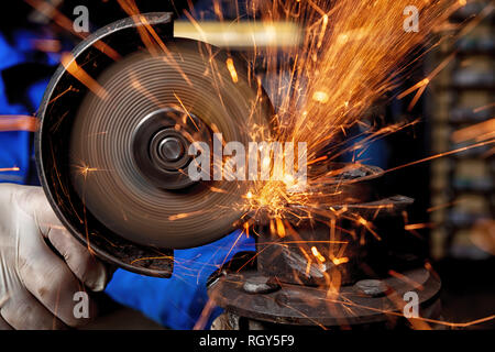 Close-up of a man sawing metal with a hand circular saw,  bright flashes flying in different directions, in the background tools for an auto repair sh Stock Photo