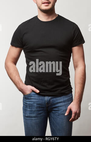 partial view of man with hand in pocket in denim and black t-shirt with copy space isolated on grey Stock Photo