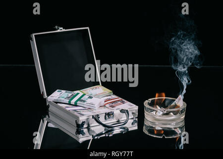 russian rubles banknotes in suitcase safe box and burning money in ashtray on black Stock Photo