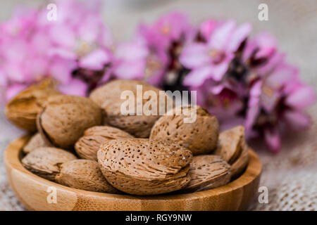 Almonds with shell in wooden bowl, with almond flowers blooming background Stock Photo