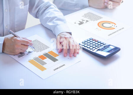 Businessmen or analyst in a meeting room partially cropped at hands holding a pen on an investment report, analysing on investment risk and a return o Stock Photo