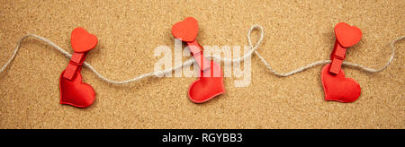 Hearts with clothespins on corkboard background, concept of uncertainty in love Stock Photo