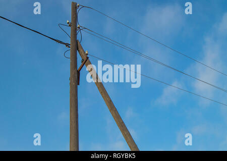 Wooden old 0.4 kV power line support with wires and insulators on blue sky background. Stock Photo