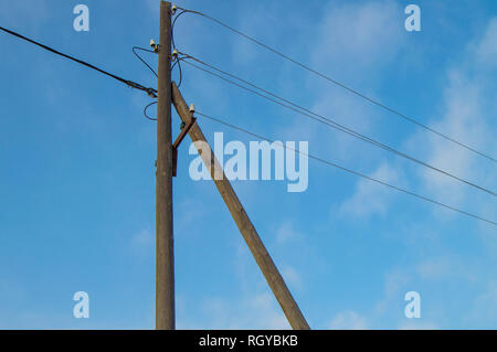 Wooden old 0.4 kV power line support with wires and insulators on blue sky background. Stock Photo
