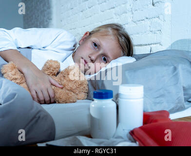 Sweet sick cute girl feeling sick lying in bed with medicines thermometer hot water bag suffering from Cold and Winter Flu Virus Sneezing Running Nose Stock Photo