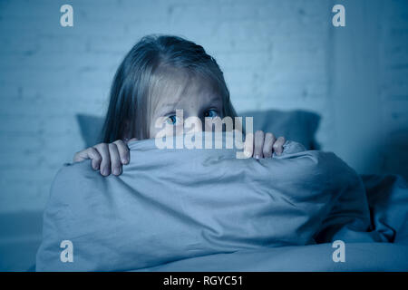 Scared little girl staying sleepless hiding behind the duvet looking horrified in the dark having childhood nightmares in child imagination Sleeping d Stock Photo