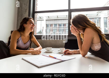 Two female colleagues laughing at work desk. Profile view. Stock Photo