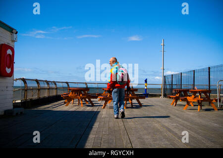 A man wearing a backpack and bright jacket walks along a pier in Blackpool. UK. Stock Photo