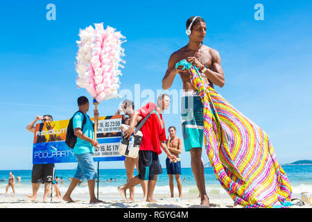 RIO DE JANEIRO - FEBRUARY, 2018: Promoters holding signs for pool parties and vendors selling candy floss walk among beachgoers on Ipanema Beach. Stock Photo