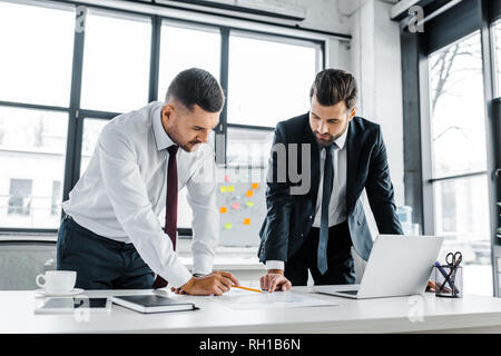 confident businessmen having discussion while standing near desk in modern office Stock Photo
