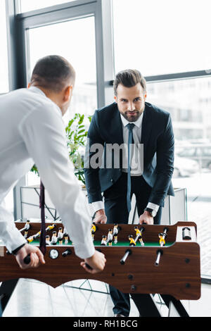bearded businessman playing table football with coworker in modern office Stock Photo