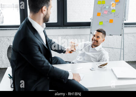 cheerful businessman clinking with alcohol drink in glass with coworker in modern office Stock Photo