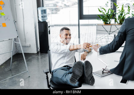smiling businessman clinking with alcohol drink in glass with coworker in modern office Stock Photo