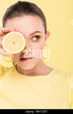 beautiful stylish girl holding lemon, biting lip and posing isolated on limelight Stock Photo