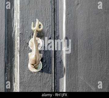 Brass door knocker in the shape of a fish mounted on a black door Stock Photo