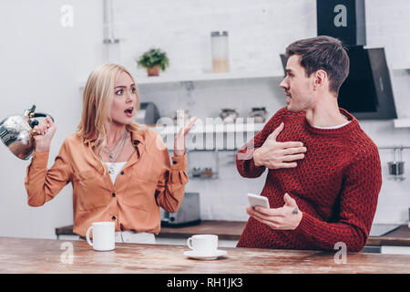 emotional young couple quarrelling in kitchen, mistrust concept Stock Photo