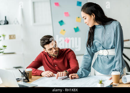 multicultural couple of architects working on blueprint in office Stock Photo
