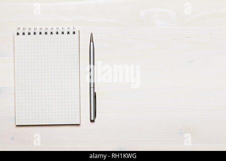 Open blank notepad with spiral and gray pen on white wooden background. Top view. Copy space Stock Photo