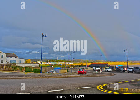 Rainbow over Porthcawl appears to end on the sunlit beach of Sandy Bay. carsPorthcawl S.Wales Stock Photo